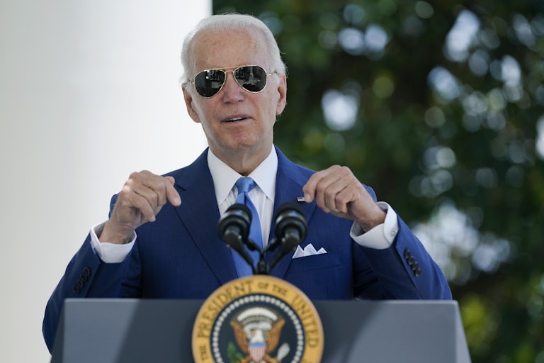 Joe Biden, wearing sunglasses, points downward towards his podium.