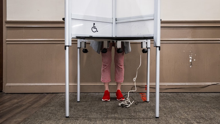 This image shows a person’s legs and feet visible beneath the polling booth as they cast their vote.