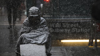 A homeless man sits in the falling snow in New York’s financial district