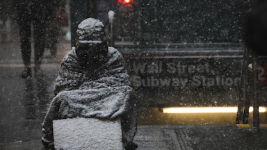 A homeless man sits in the falling snow in New York’s financial district