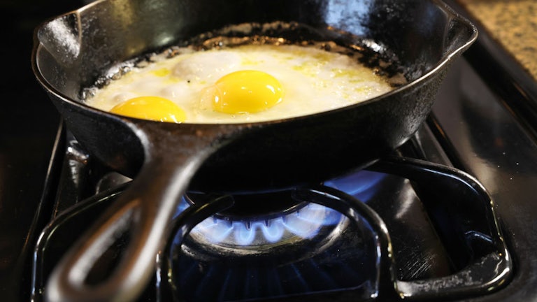 Two eggs fry in a cast-iron pan on a gas burner.