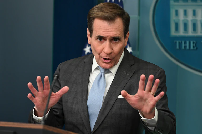 John Kirby speaks and splays his hands out as if in anger. He is giving a press briefing judging by the White House logo in the background.
