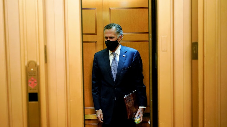 A masked Mitt Romney stands alone in an elevator.