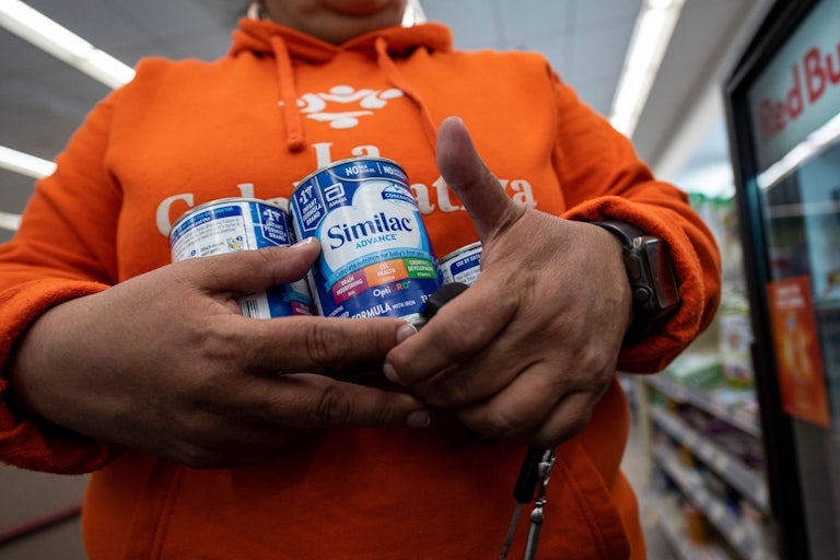 A person holds cans of Similac baby formula.