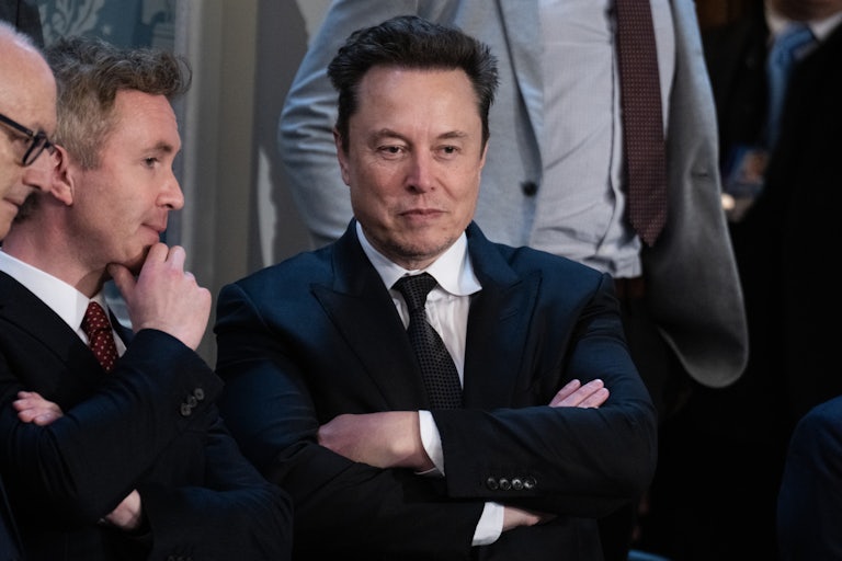Elon Musk stands with his arms crossed