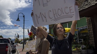 A teenage girl in the foreground holds a sign that reads "My Body My Choice!" Another in the background holds a sign that says "Wombs Are Not State Property."
