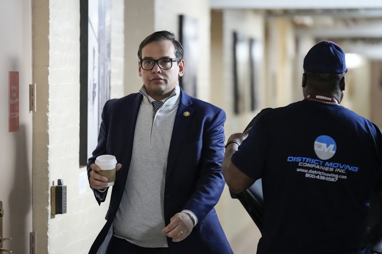 George Santos walks down a hallway with a coffee cup in his hand