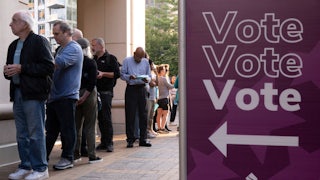People stand next to a sign reading "Vote Vote Vote."
