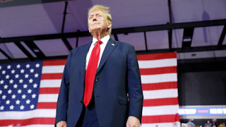 Donald Trump stands in front of a large U.S. flag.