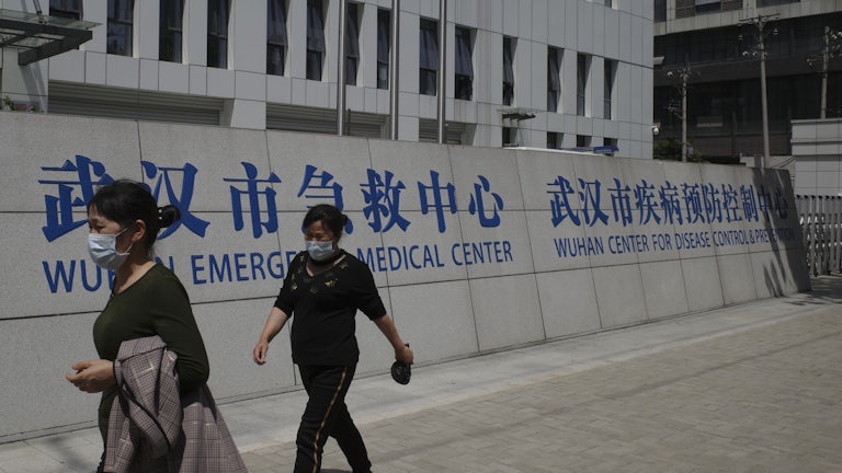 People walk past a building labeled “Wuhan Emergency Medical Center” and “Wuhan Center for Disease Control and Prevention.”