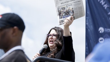 A woman holds up a copy of The New York Times reading "Roe Overturned."