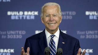 A close-up of a smiling Joe Biden standing behind a lectern.