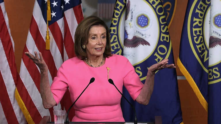 Nancy Pelosi stands behind a lectern shrugging at a press conference on Capitol Hill.
