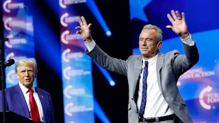 Robert F. Kennedy Jr. walks forward with his hands raised, as Trump stands to the side.