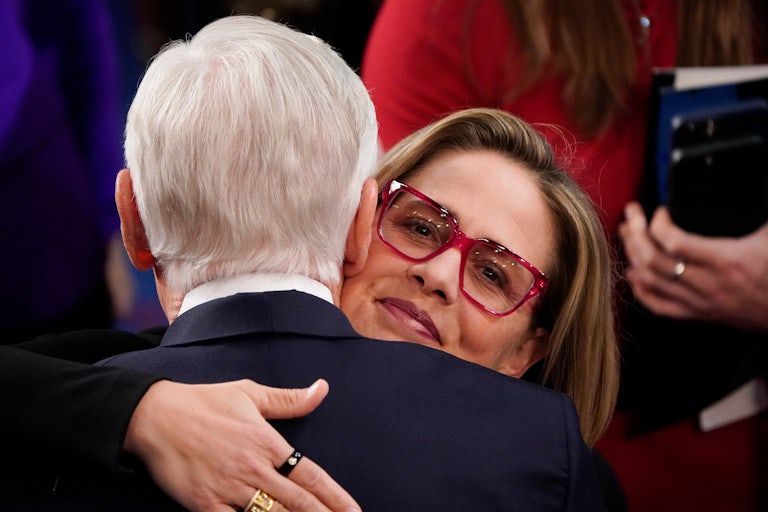 Senator Kyrsten Sinema hugs an old white man in a suit (we can only see their back)