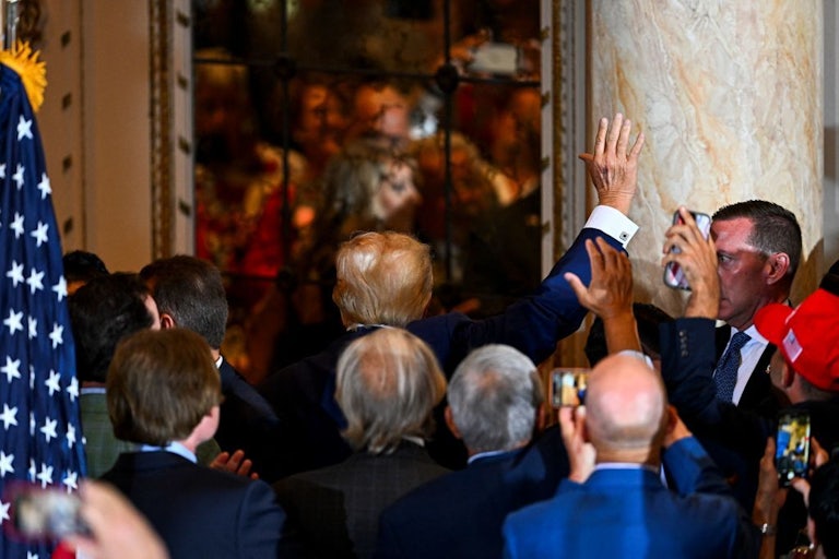 Donald Trump walks away from the camera out of a room, while waving.