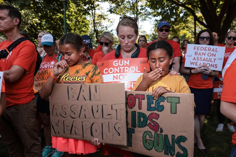 Protesters hold signs that read "Ban assault weapons" and "Protect kids, not guns."