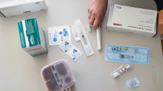 A hand hovers over an assortment of syringes, vials of fertility drugs, and alcohol wipes.