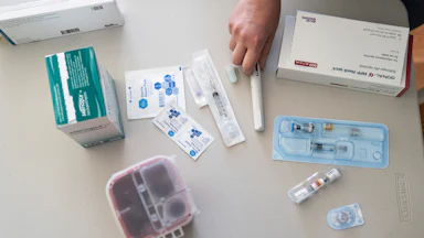 A hand hovers over an assortment of syringes, vials of fertility drugs, and alcohol wipes.