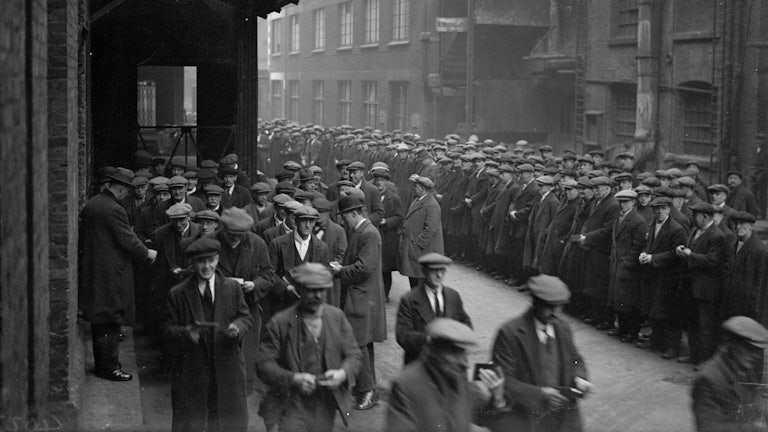 A large quantity of men stand assembled in a dockyard.