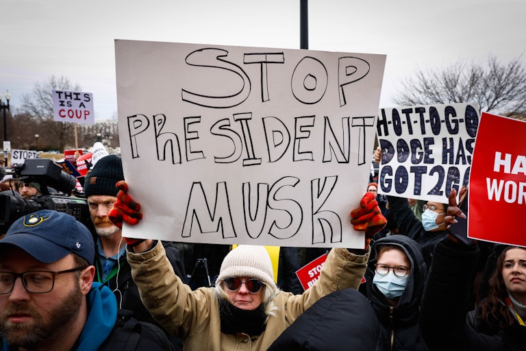 People hold up signs at a protest against Elon Musk outside the Department of Labor in Washington, D.C.