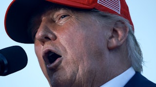 Donald Trump speaks into a mic while wearing a MAGA hat