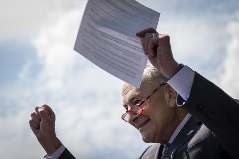 Chuck Schumer holds a paper above his head, smiling.