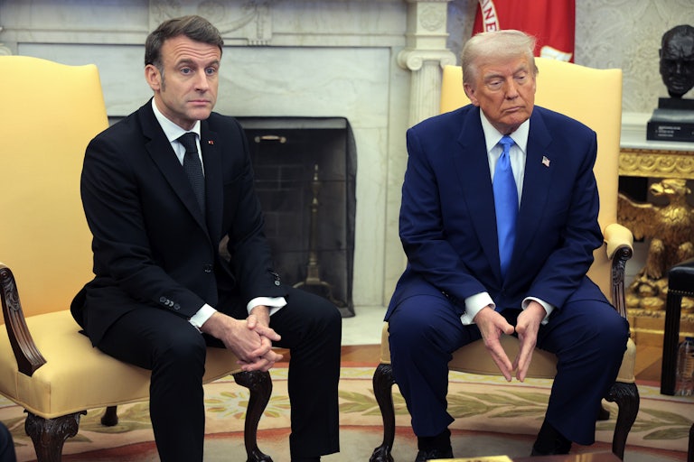 French President Emmanuel Macron looks shocked while sitting in a chair next to Donald Trump in the White House.