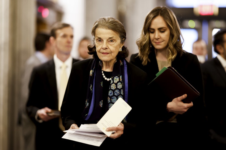 Senator Dianne Feinstein walks down a hallway, papers in hand.