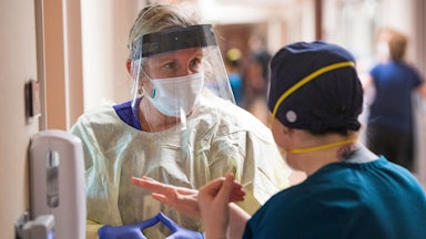 a nurse wearing a mask and face shield talks to another nurse in a Covid ICU