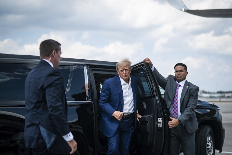 Donald Trump exits a car as someone opens a door for him.