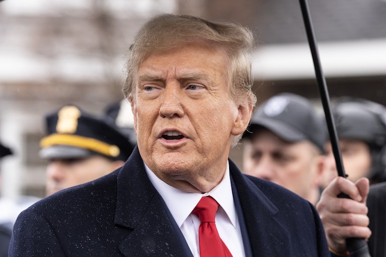 Donald Trump looks to the side as he stands under an umbrella
