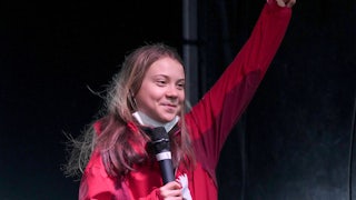 Greta Thunberg raises her fist, smiling.