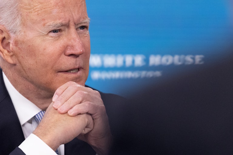 A close up of President Joe Biden, speaking with hands folded under his chin.