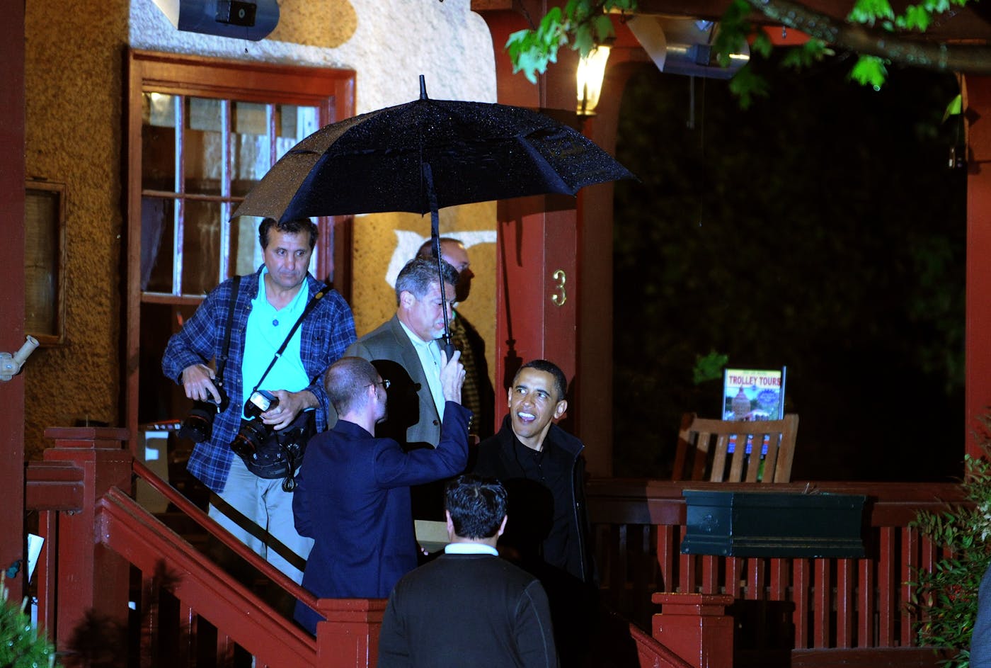 Barack Obama walks down porch stairs at night surrounded by other people.