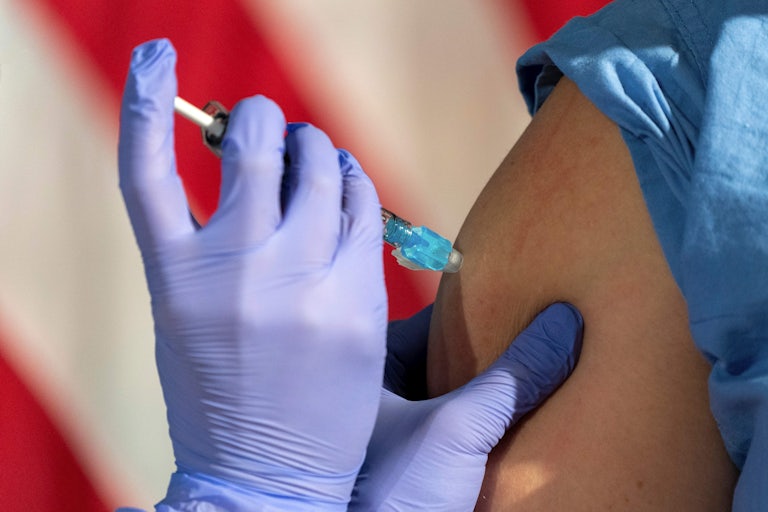 Close-up of a nurse administering a Covid vaccine in front of an American flag.