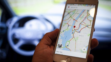 A hand holds a mobile phone displaying a Google Maps application.
