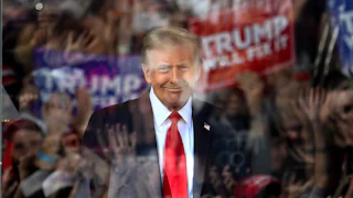 Trump is seen through bulletproof glass with the reflections of cheering fans in the glass.