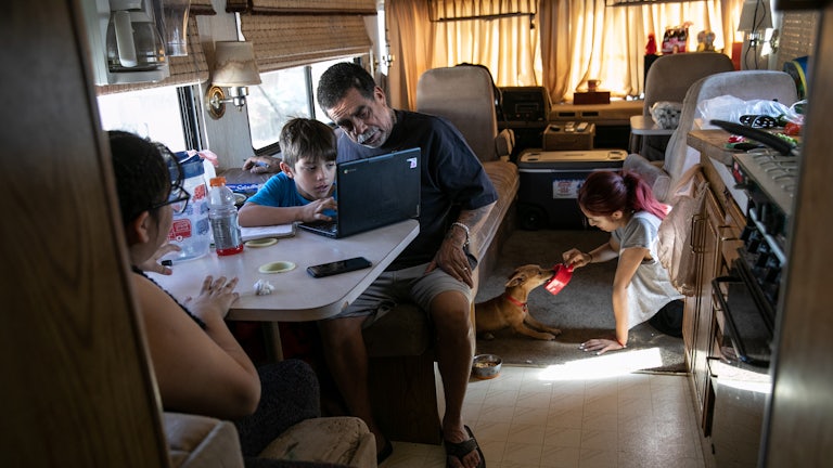 Inside an RV, a father helps his son with homework while his two daughters sit nearby. 