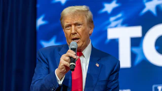 Donald Trump, seated, speaks with a mic in his hand