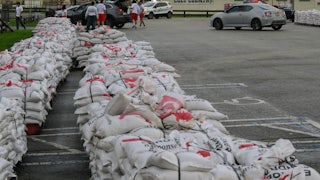 Two rows of sandbags piled up in a parking lot. A building in the back reads "Welcome to Colt County."