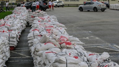Two rows of sandbags piled up in a parking lot. A building in the back reads "Welcome to Colt County."