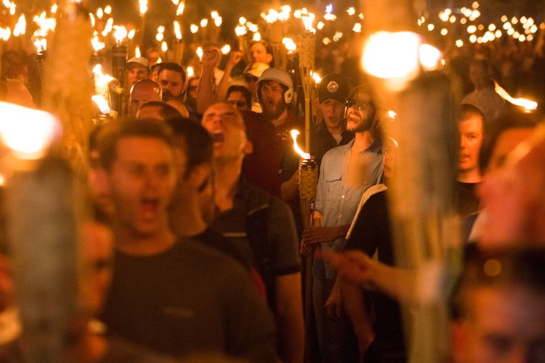 Young white men hold tiki torches and shout