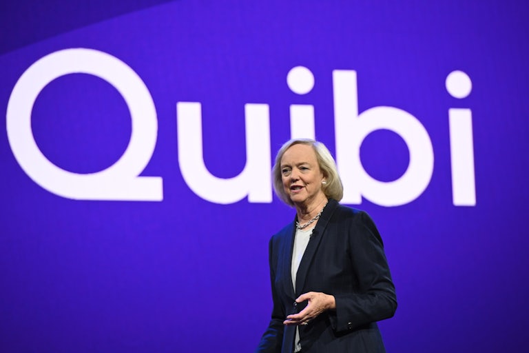 Quibi CEO Meg Whitman stands before a banner that reads “Quibi”