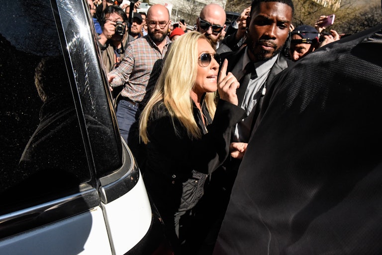 Marjorie Taylor Greene wags her finger amid a crowd of people, including reporters