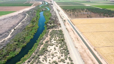 A river flows between farm fields, with green vegetation along its banks.