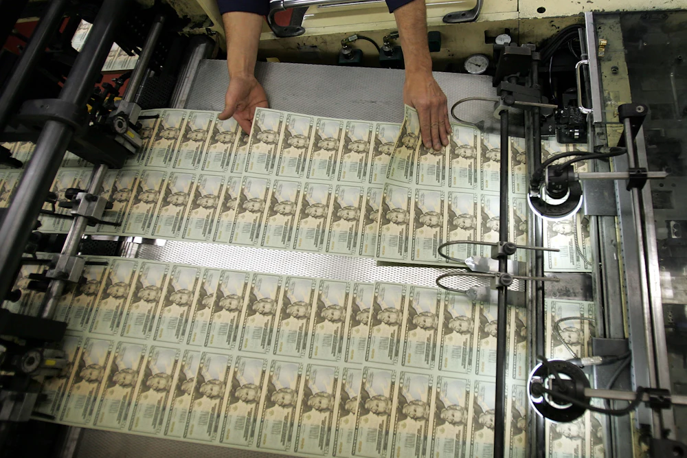 A worker's hands hover over recently printed twenty-dollar bills, inspecting them.