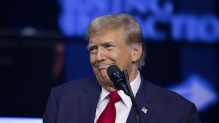 Donald Trump smiles weirdly at something off camera. A mic stands before him.