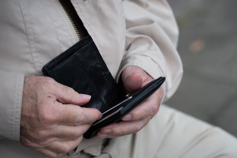 An elderly person holds a wallet