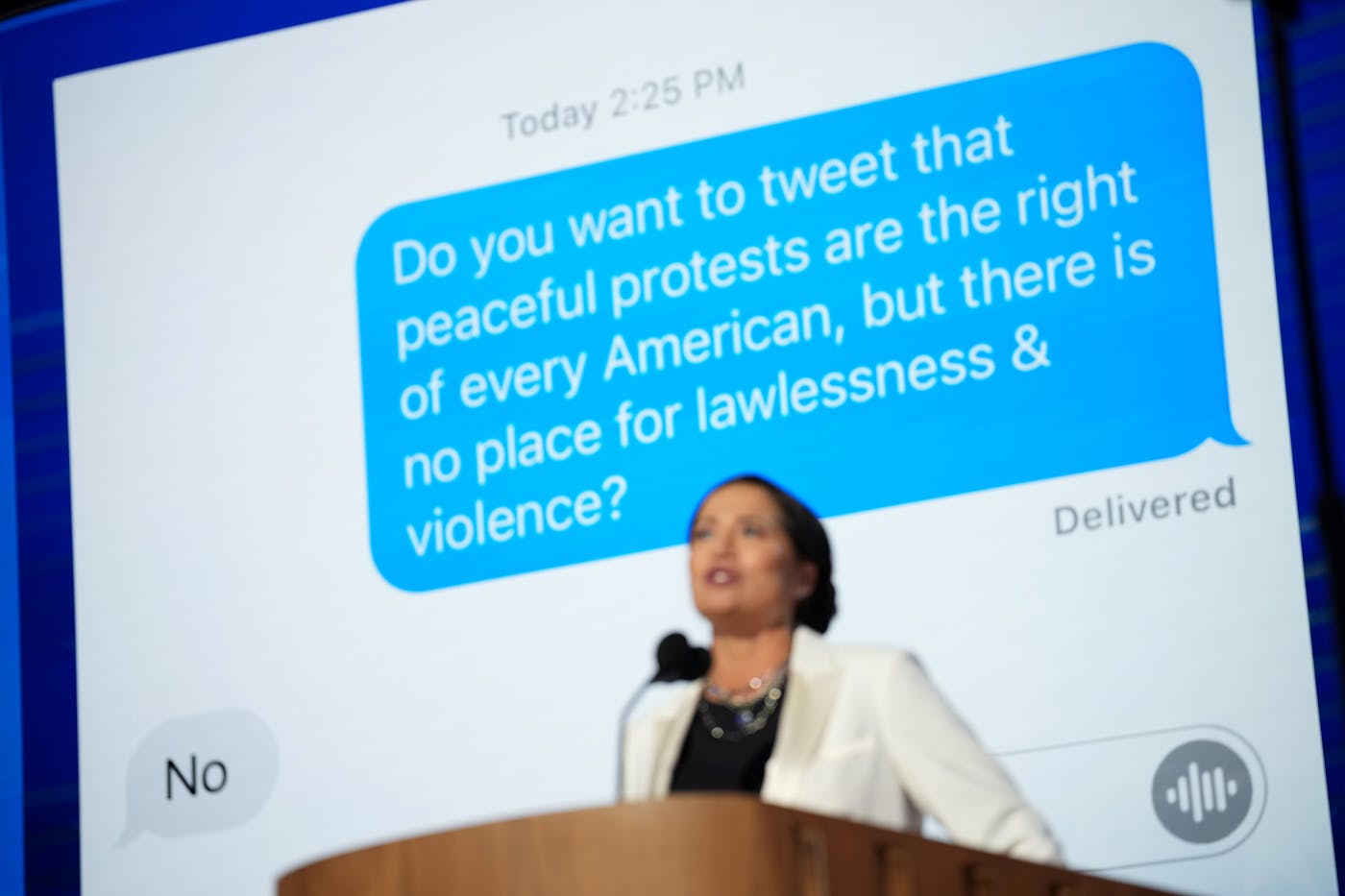 Stephanie Grisham speaks at the DNC with the two texts behind her on a giant screen